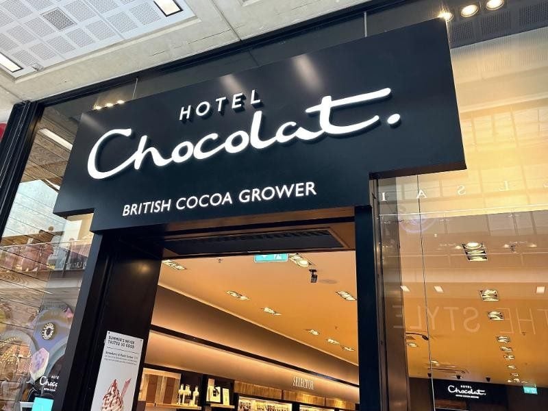 A Hotel Chocolat shop front with its lit sign reading British cocoa grower