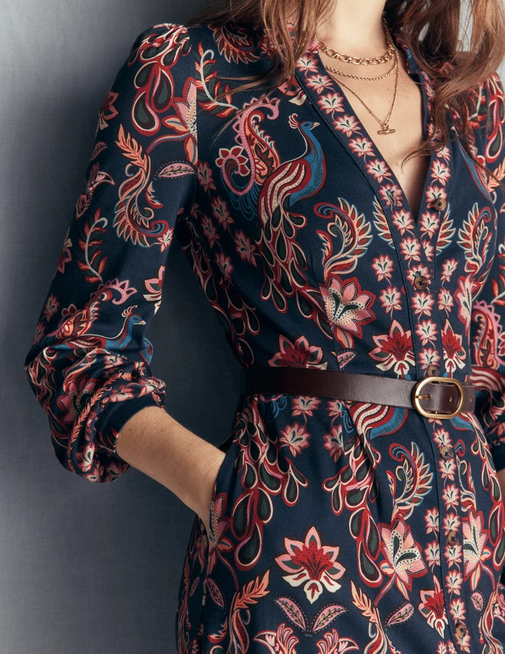 A model in a Boden peacock-print shirt dress with a brown leather belt